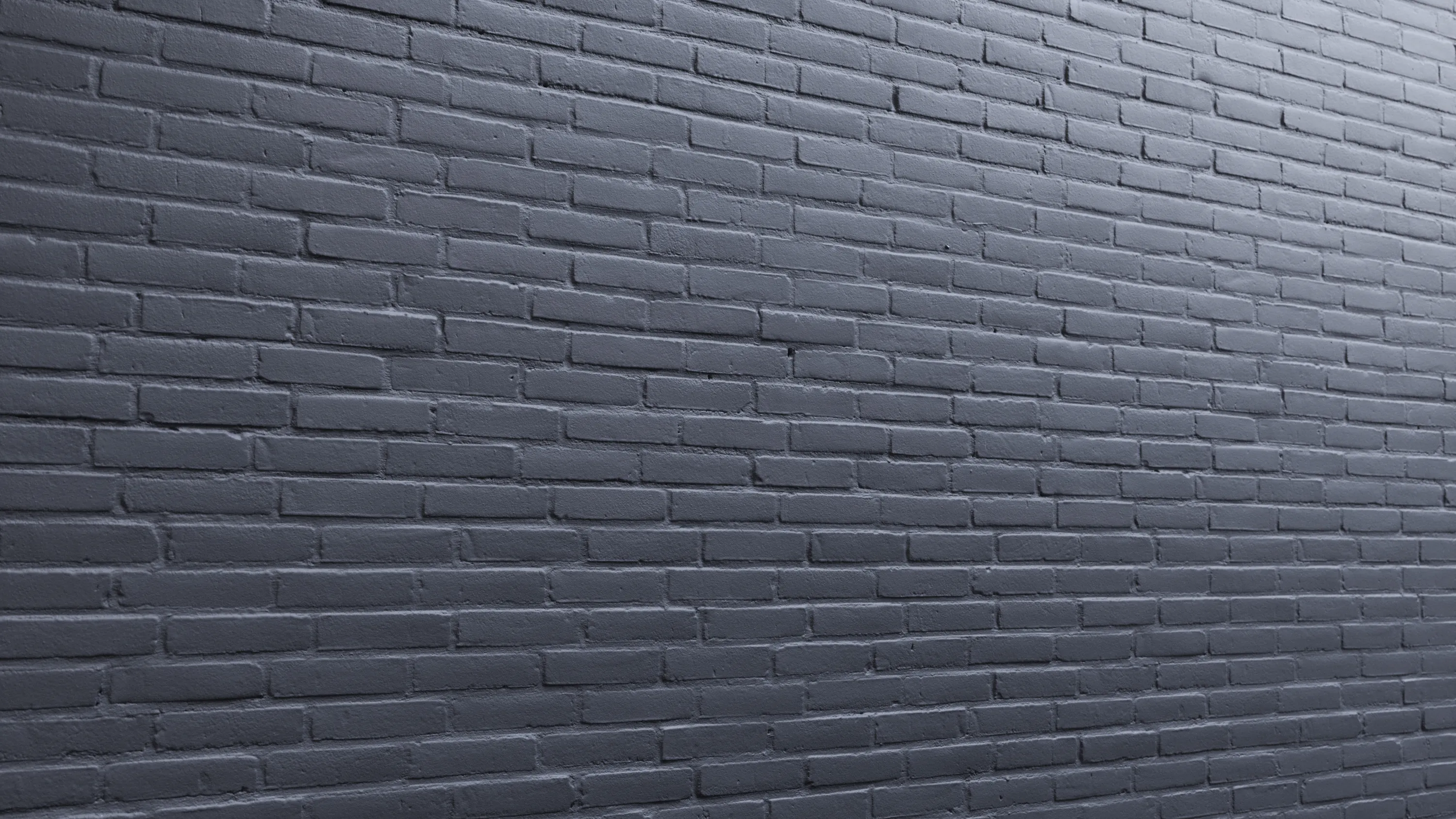 Harmaa tiiliseinä, jossa on vaakasuoria tiiliä ja tasainen valaistus.